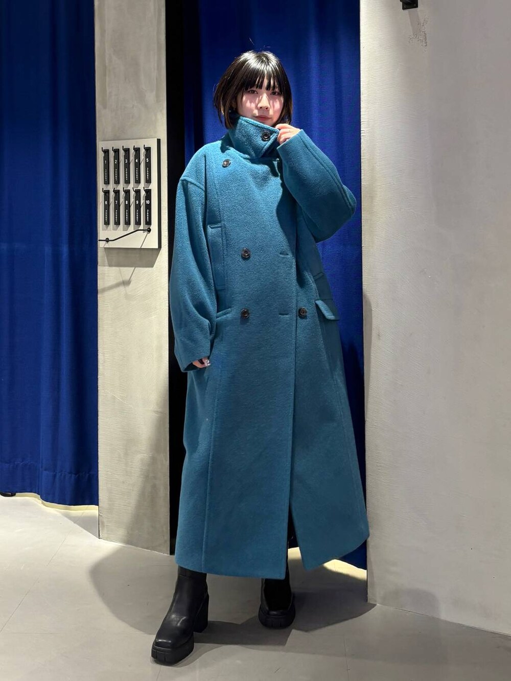 グリーン系のチェスターコート、ブラック系のブーツ、グレー系のニット/セーターを着用したレディースの冬コーディネートの6枚目の写真