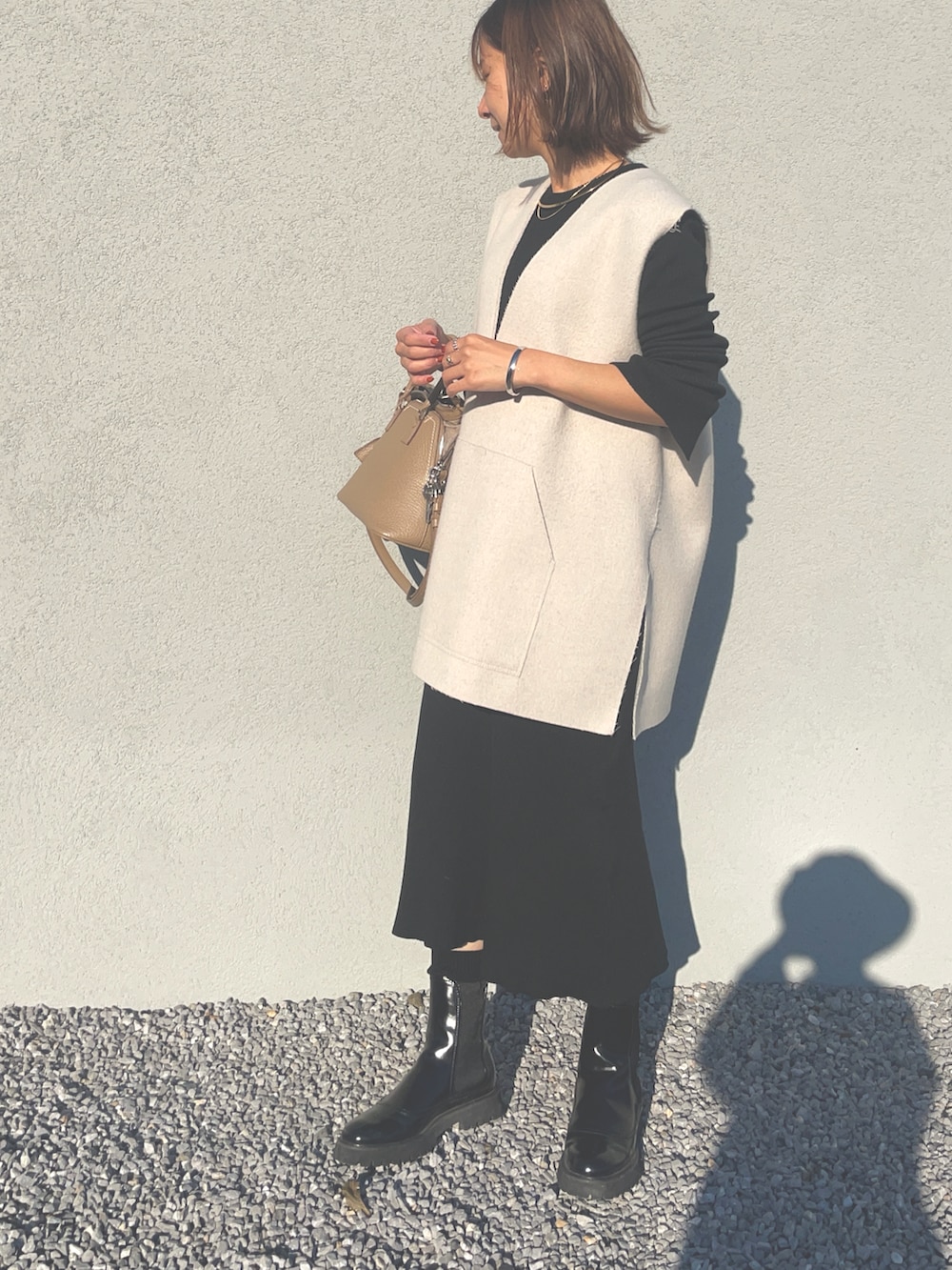 ベージュ系のベスト、ブラック系のワンピース、ブラック系のブーツを着用したレディースの冬コーディネートの2枚目の写真