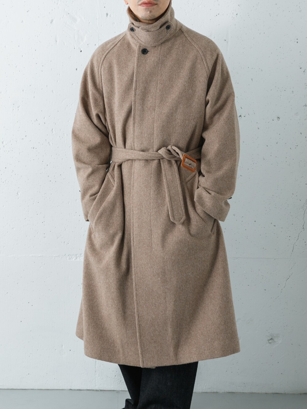 ブラック系のデニムパンツ、ベージュ系のステンカラーコート、グリーン系のニット/セーターを着用したメンズの冬コーディネートの2枚目の写真