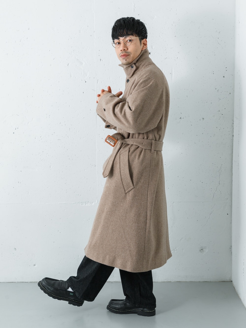 ブラック系のデニムパンツ、ベージュ系のステンカラーコート、グリーン系のニット/セーターを着用したメンズの冬コーディネートの3枚目の写真