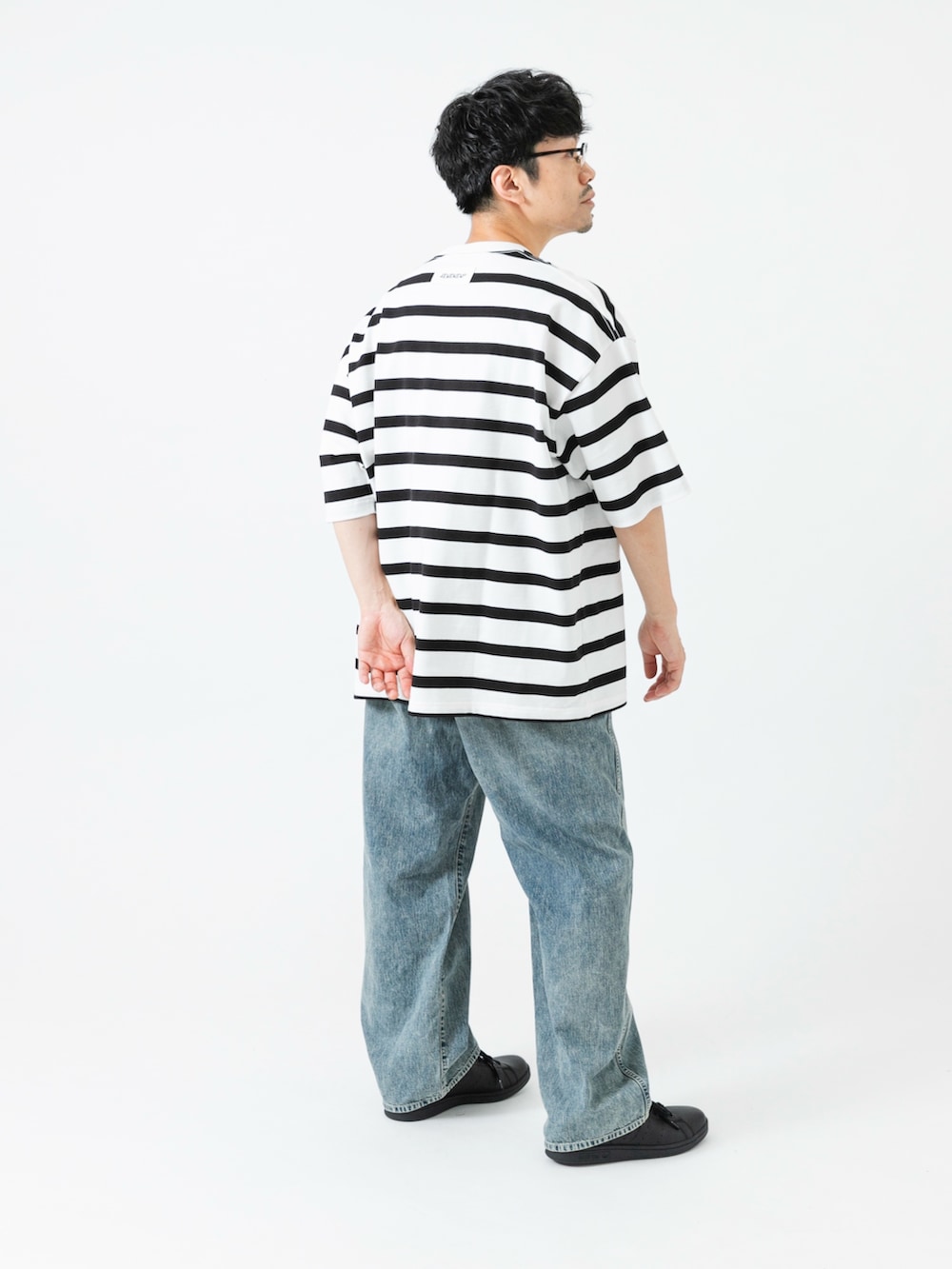 ブラック系のスニーカー、ホワイト系のTシャツ/カットソー、ブルー系のデニムパンツを着用したメンズの夏コーディネートの5枚目の写真