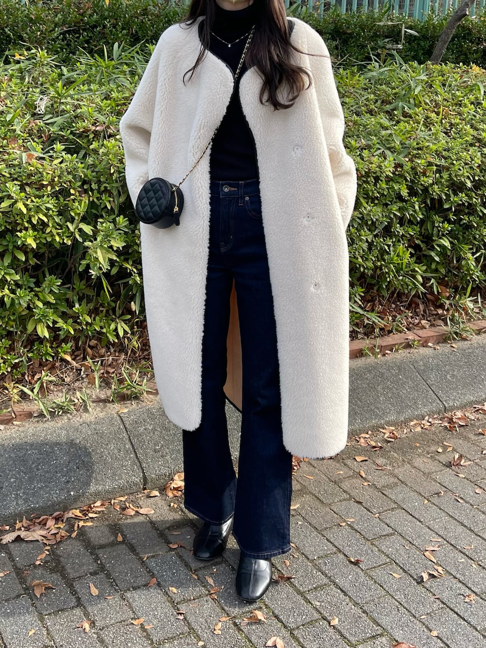 ホワイト系のノーカラーコート、ブラック系のニット/セーター、ブルー系のデニムパンツを着用したレディースの冬コーディネートの2枚目の写真