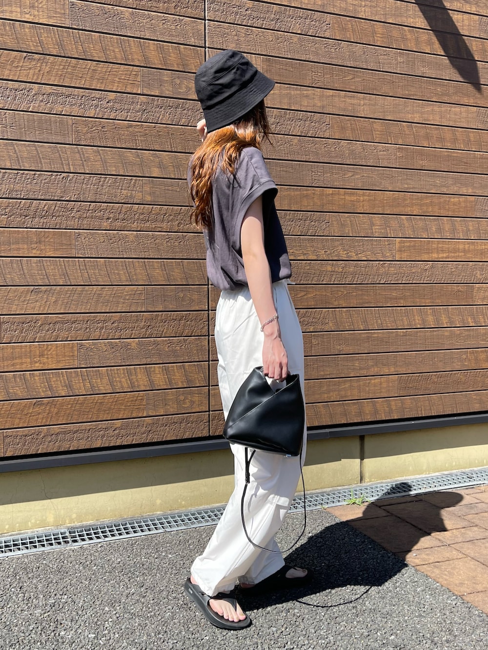 グレー系のトップス、ホワイト系のパンツ、ブラック系のサンダルを着用したレディースの夏コーディネートの2枚目の写真