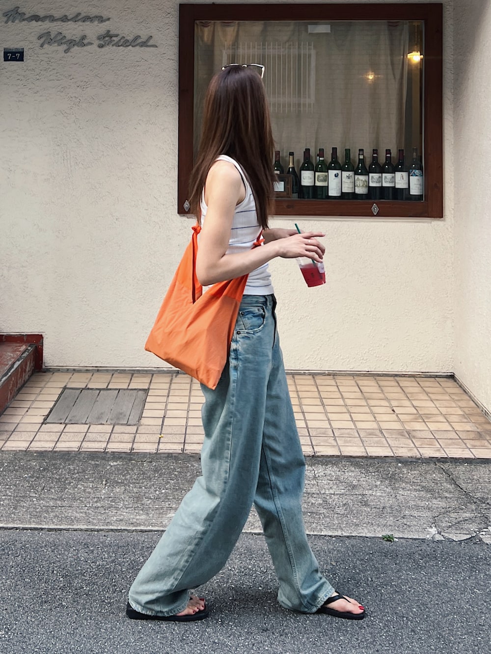 ホワイト系のキャミソール、オレンジ系のバッグ、ブルー系のデニムパンツを着用したレディースの夏コーディネートの2枚目の写真