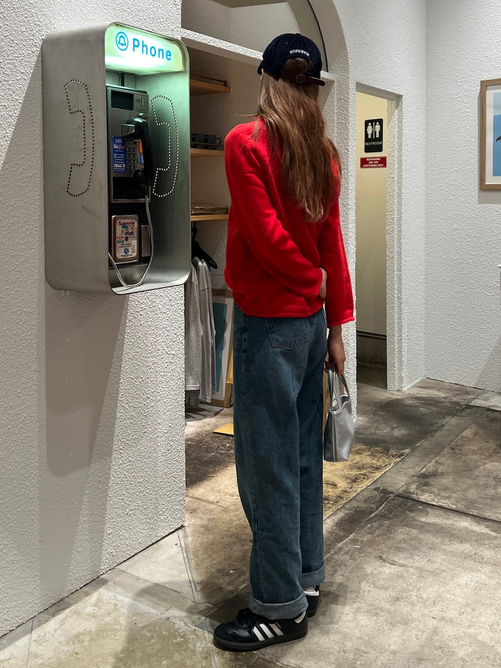 レッド系のニット/セーター、ブルー系のデニムパンツ、シルバー系のショルダーバッグを着用したレディースの秋コーディネートの2枚目の写真