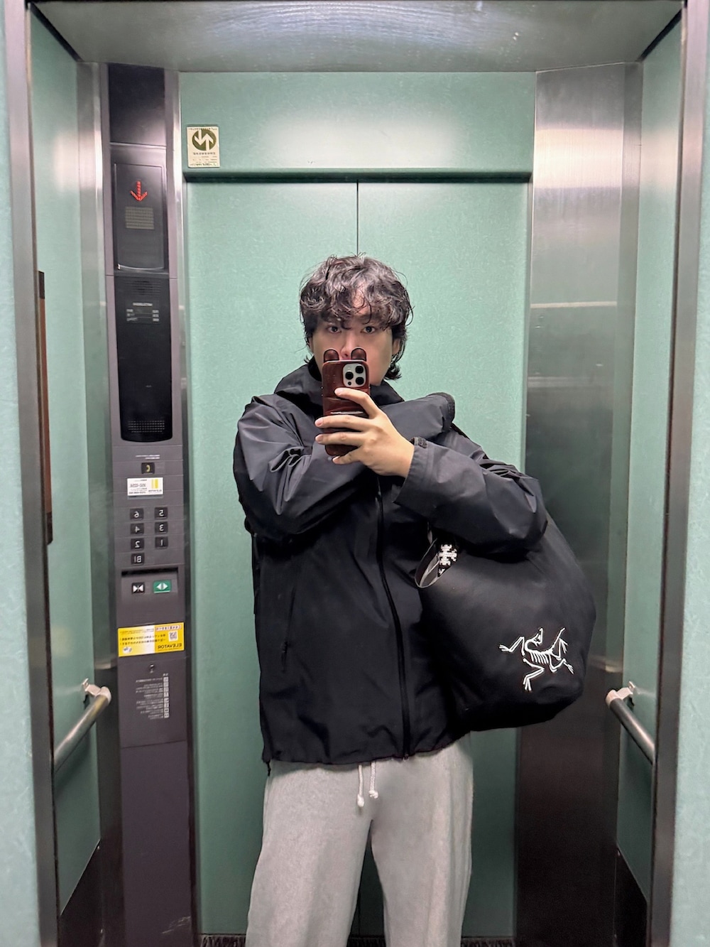 ブラック系のトートバッグ、ブラック系のマウンテンパーカー、ブラウン系のスニーカーを着用したメンズの冬コーディネートの5枚目の写真