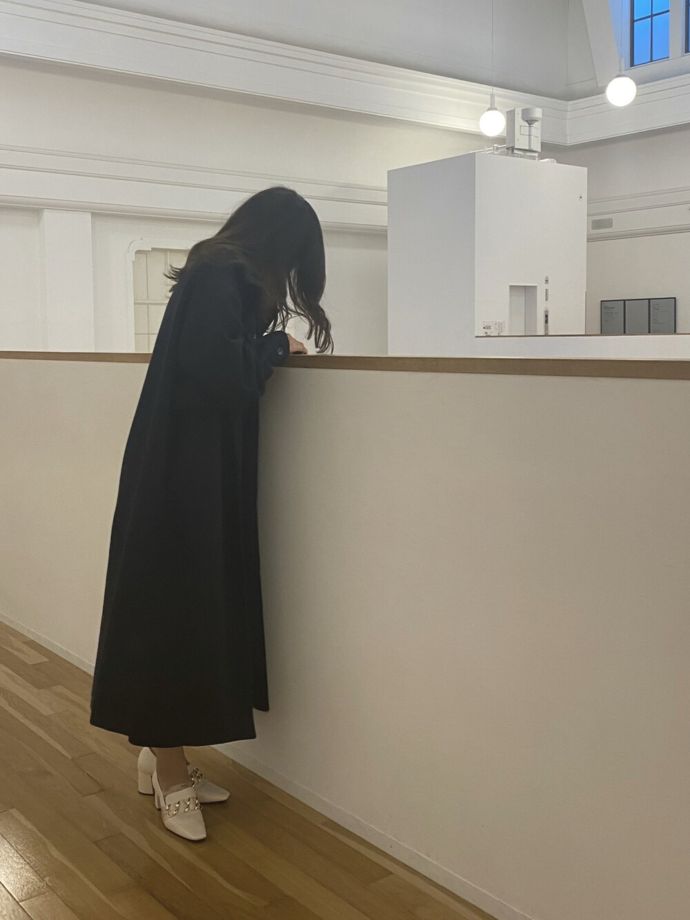 ブラック系のステンカラーコート、イエロー系のニット/セーター、ブラック系のスカートを着用したレディースの冬コーディネートの3枚目の写真