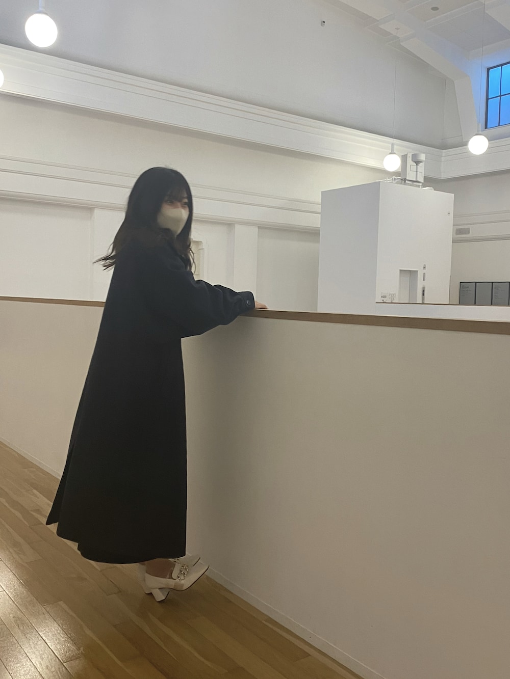 ブラック系のステンカラーコート、イエロー系のニット/セーター、ブラック系のスカートを着用したレディースの冬コーディネートの2枚目の写真