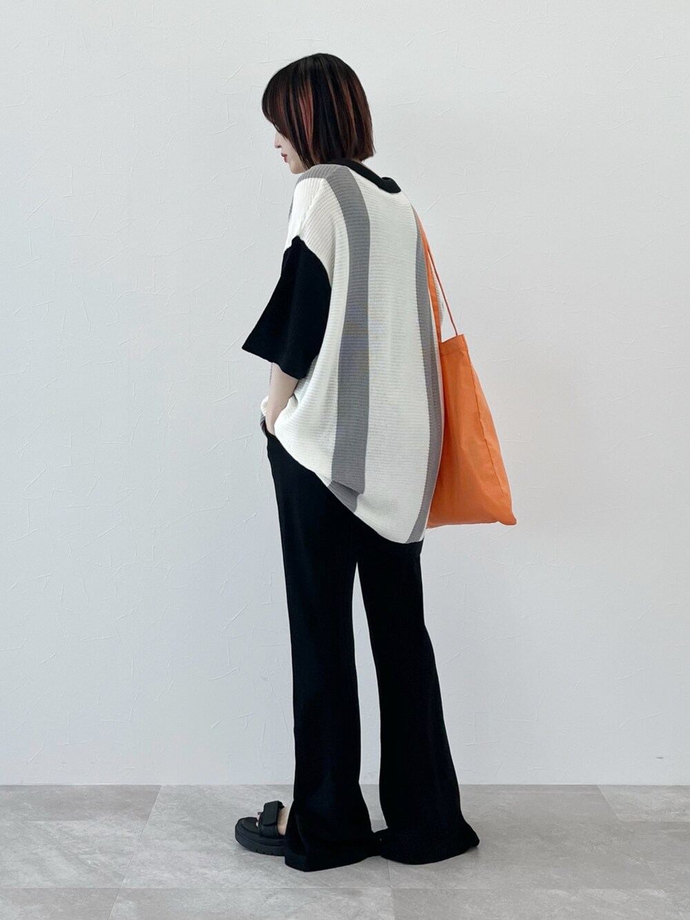 ブラック系のニット/セーター、オレンジ系のショルダーバッグ、ブラック系のスラックスを着用したレディースの春コーディネートの3枚目の写真