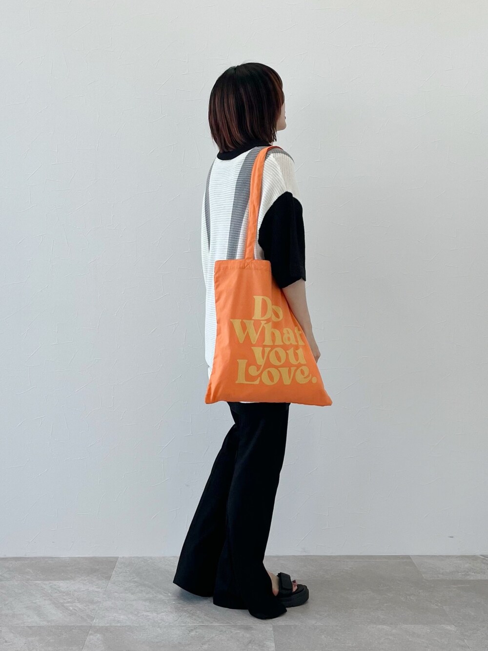 ブラック系のニット/セーター、オレンジ系のショルダーバッグ、ブラック系のスラックスを着用したレディースの春コーディネートの4枚目の写真