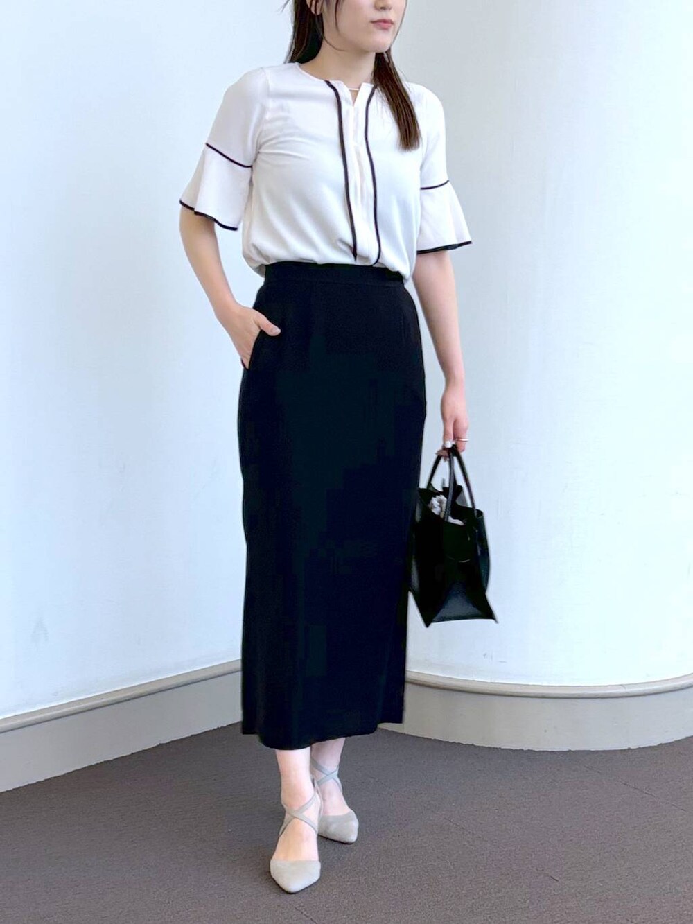 ブラック系のトートバッグ、グレー系のパンプス、ホワイト系のシャツ/ブラウスを着用したレディースの春コーディネートの2枚目の写真