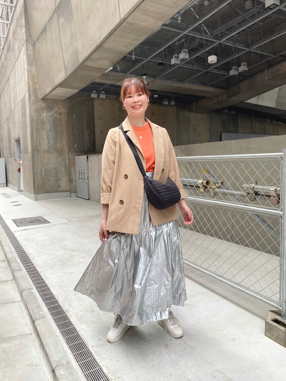シルバー系のスカート、オレンジ系のTシャツ/カットソー、ベージュ系のピーコートを着用したレディースの秋コーディネートの2枚目の写真