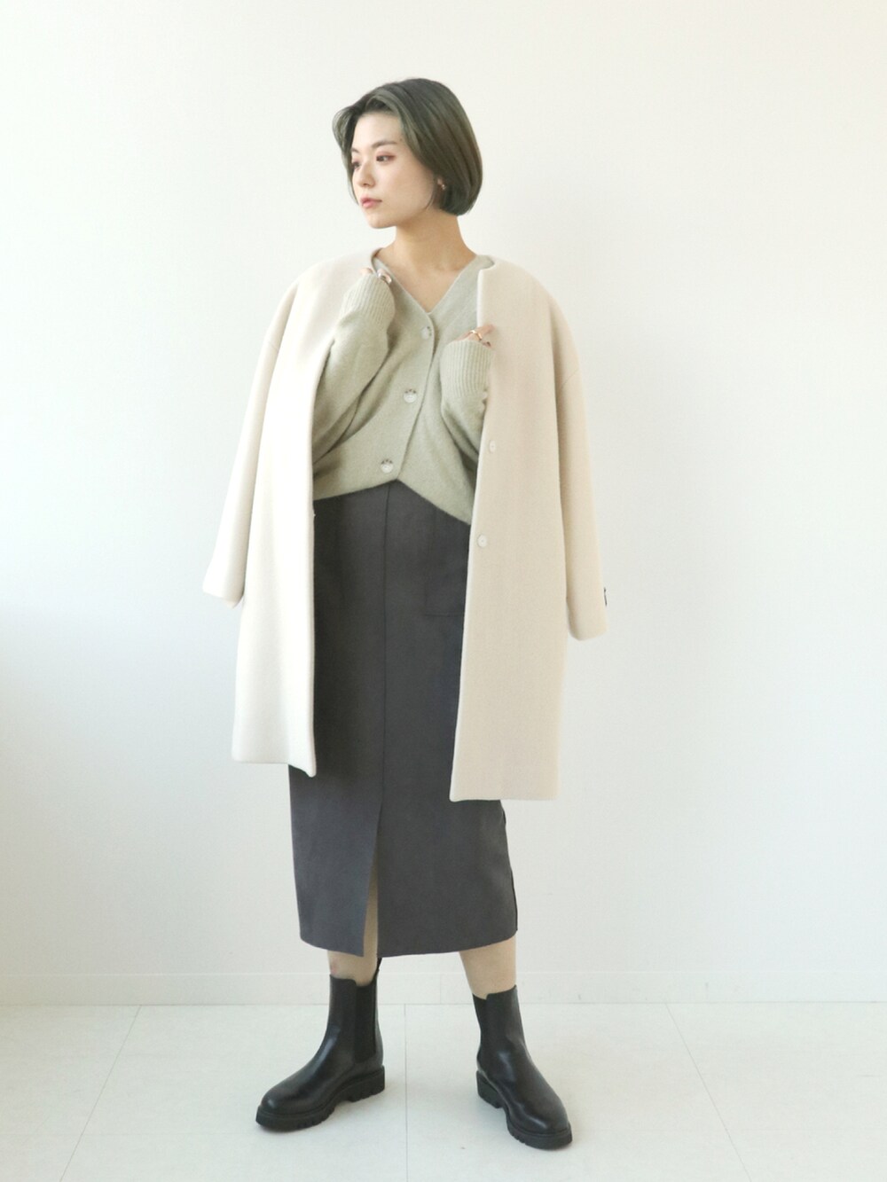 ホワイト系のノーカラーコート、ベージュ系のカーディガン/ボレロ、グレー系のスカートを着用したレディースの秋コーディネートの3枚目の写真