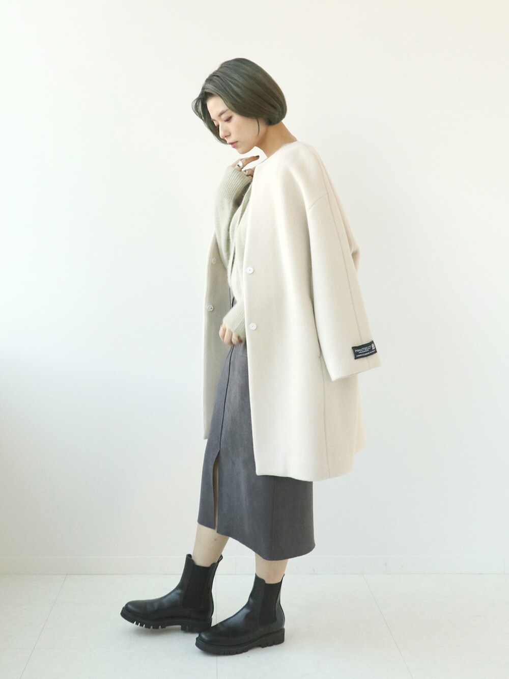 ホワイト系のノーカラーコート、ベージュ系のカーディガン/ボレロ、グレー系のスカートを着用したレディースの秋コーディネートの2枚目の写真