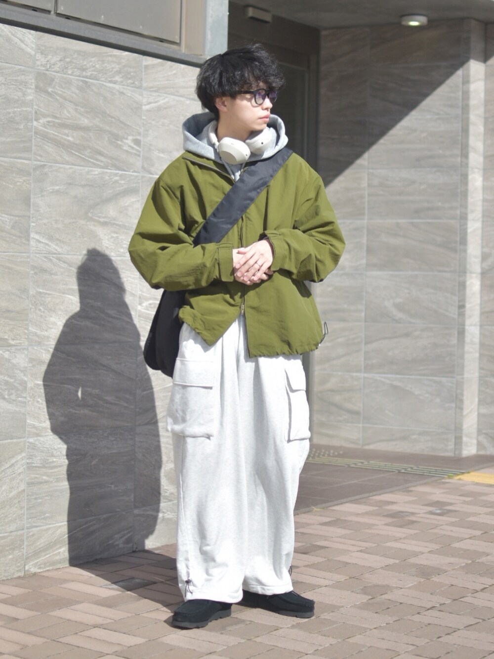 グリーン系のナイロンジャケット、ブラック系のショルダーバッグ、ホワイト系のパンツを着用したメンズの冬コーディネートの2枚目の写真