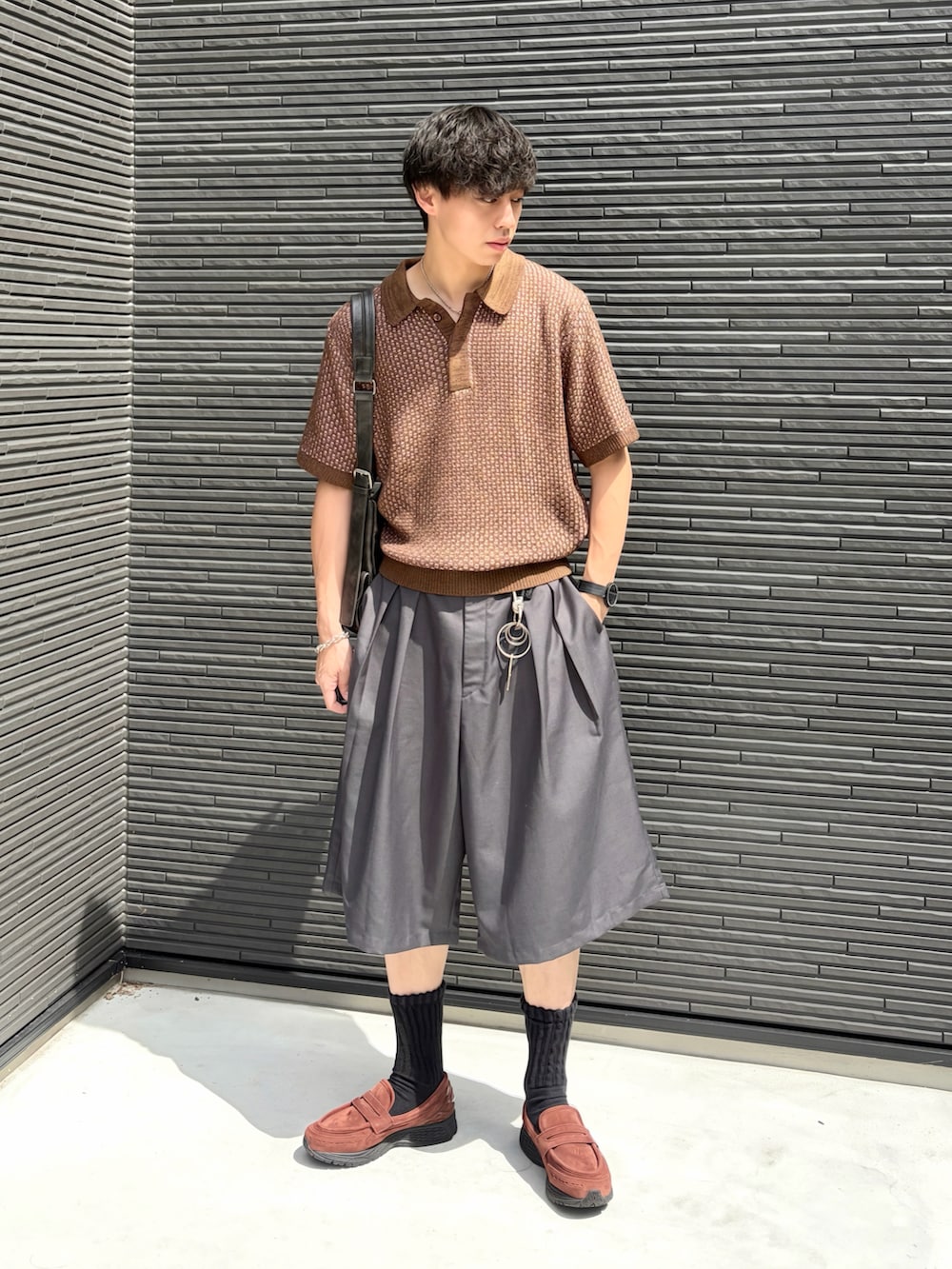 ブラック系のショルダーバッグ、ブラウン系のポロシャツ、グレー系のスラックスを着用したメンズの夏コーディネートの2枚目の写真