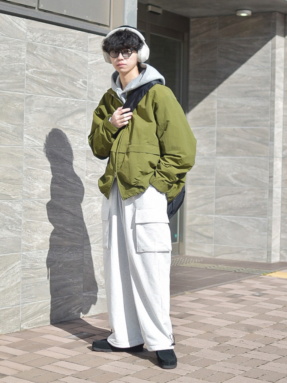 グリーン系のナイロンジャケット、ブラック系のショルダーバッグ、ホワイト系のパンツを着用したメンズの冬コーディネートの3枚目の写真