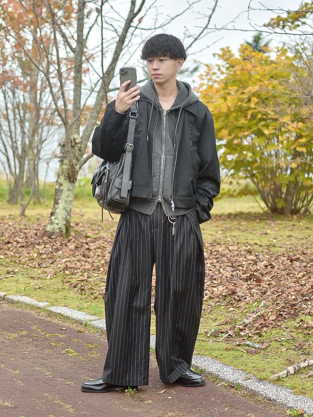 グレー系のパーカー、ブラック系のブルゾン、ブラック系のスラックスを着用したメンズの秋コーディネートの2枚目の写真