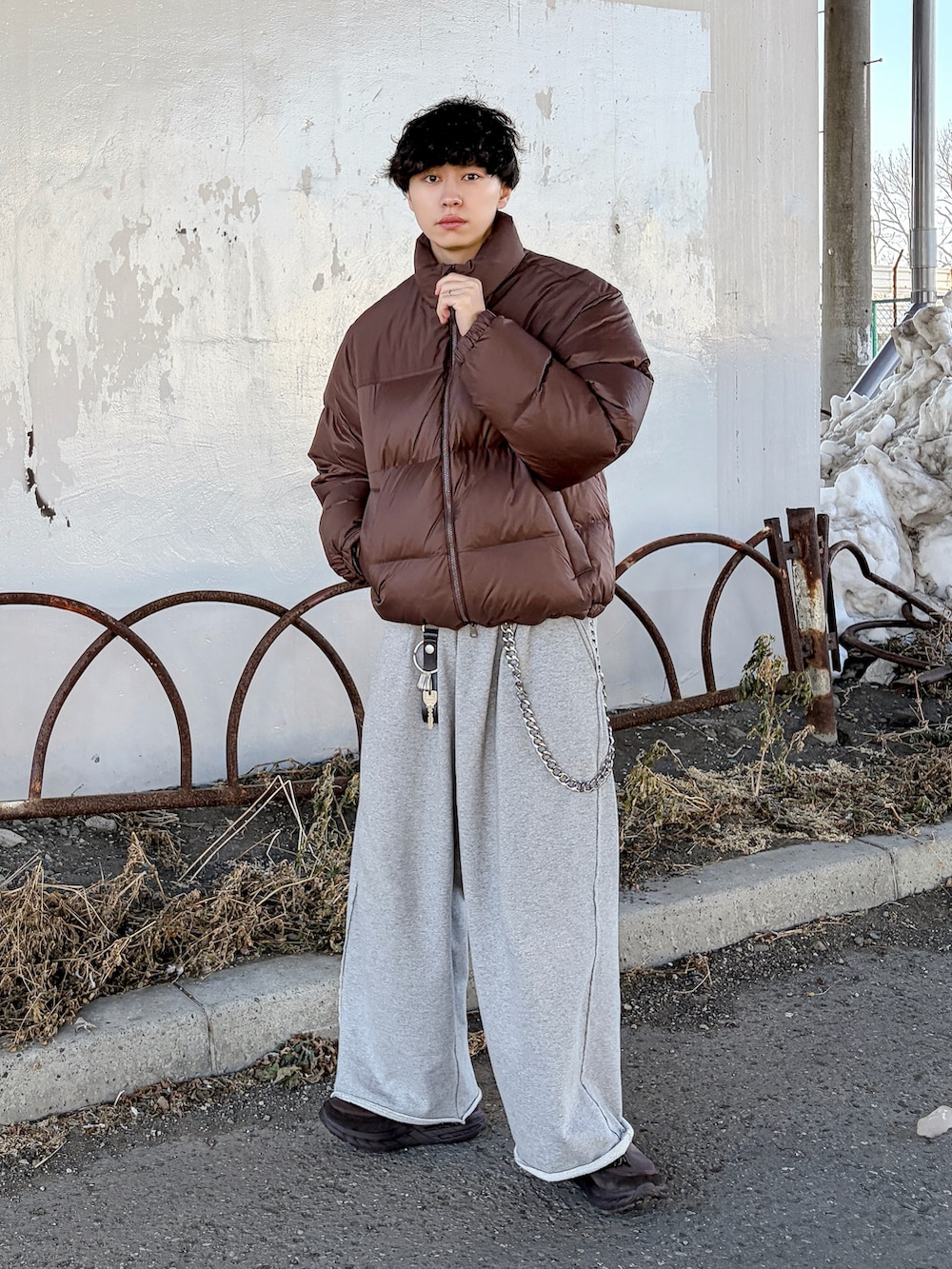 ブラウン系のダウンジャケット/コート、ブラウン系のニット/セーター、グレー系のスウェットパンツを着用したメンズの冬コーディネートの2枚目の写真