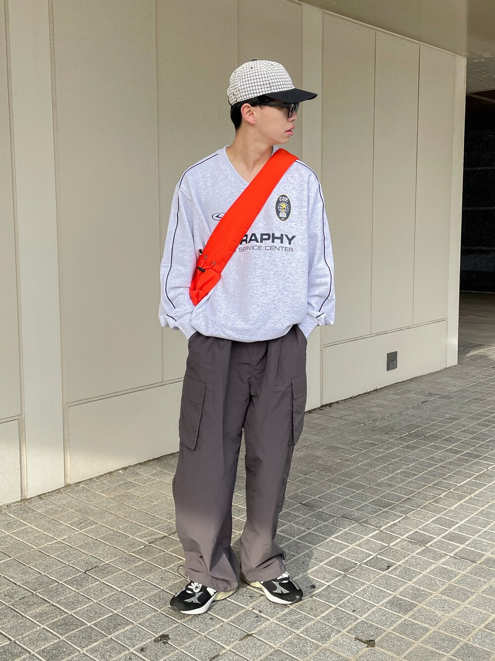グレー系のスウェット、グレー系のカーゴパンツ、オレンジ系のショルダーバッグを着用したメンズの春コーディネートの3枚目の写真