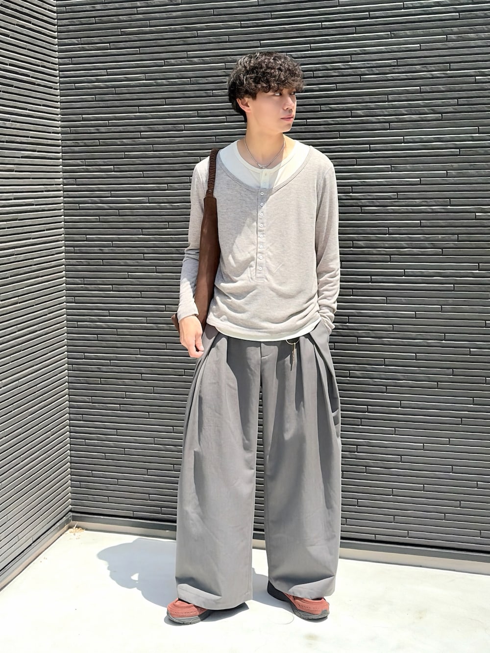 ブラウン系のトートバッグ、グレー系のTシャツ/カットソー、グレー系のスラックスを着用したメンズの夏コーディネートの2枚目の写真