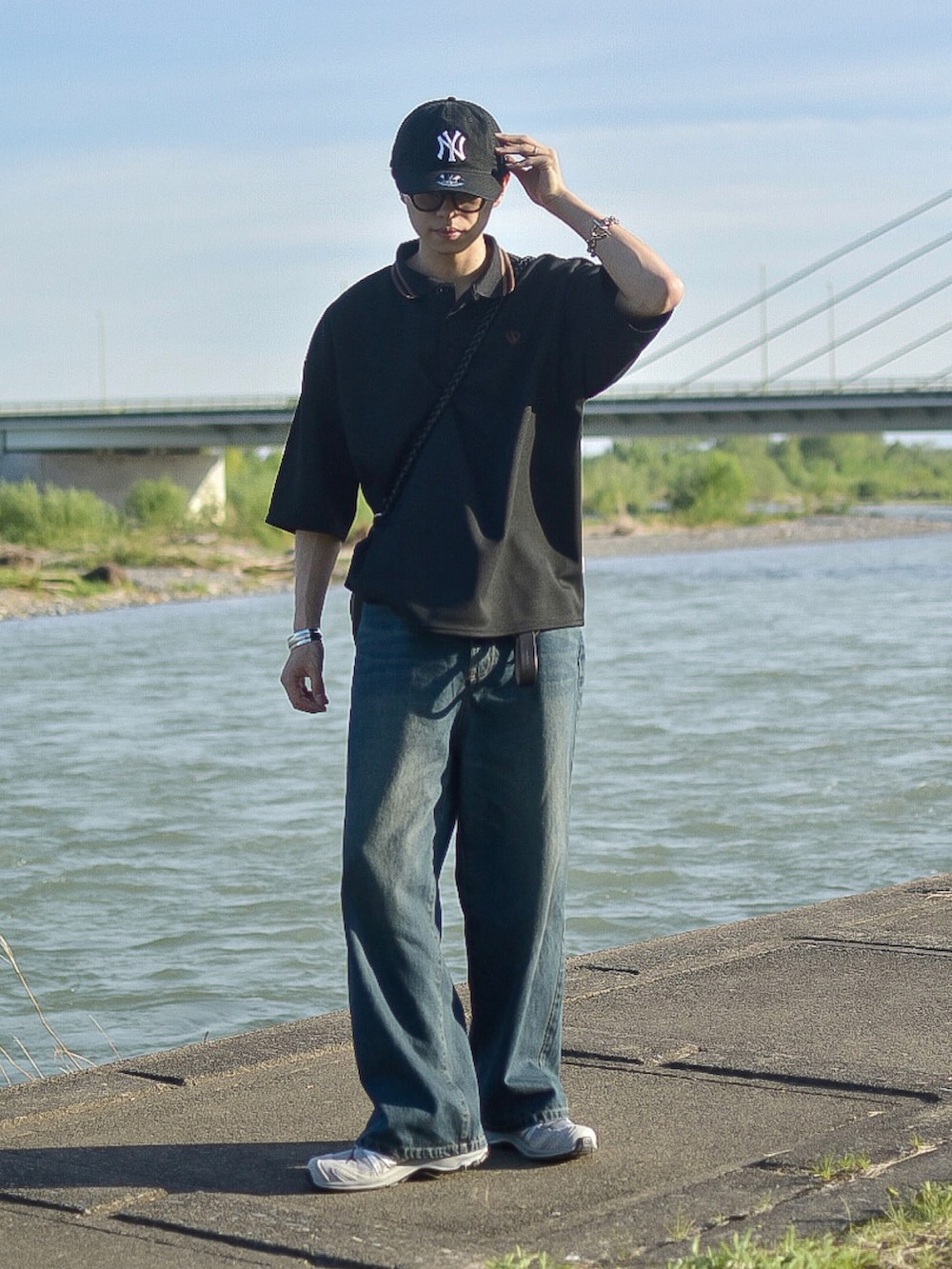 ブラック系のポロシャツ、ブルー系のデニムパンツ、ブラック系のショルダーバッグを着用したメンズの春コーディネートの3枚目の写真