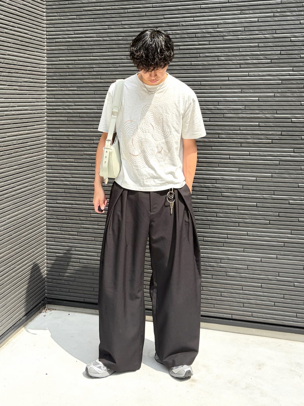 ホワイト系のTシャツ/カットソー、ブラック系のスラックス、グレー系のスニーカーを着用したメンズの夏コーディネートの3枚目の写真