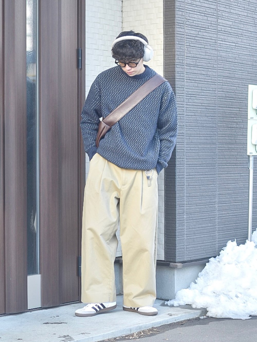 ブルー系のニット/セーター、ホワイト系のスニーカー、ブラウン系のショルダーバッグを着用したメンズの冬コーディネートの2枚目の写真