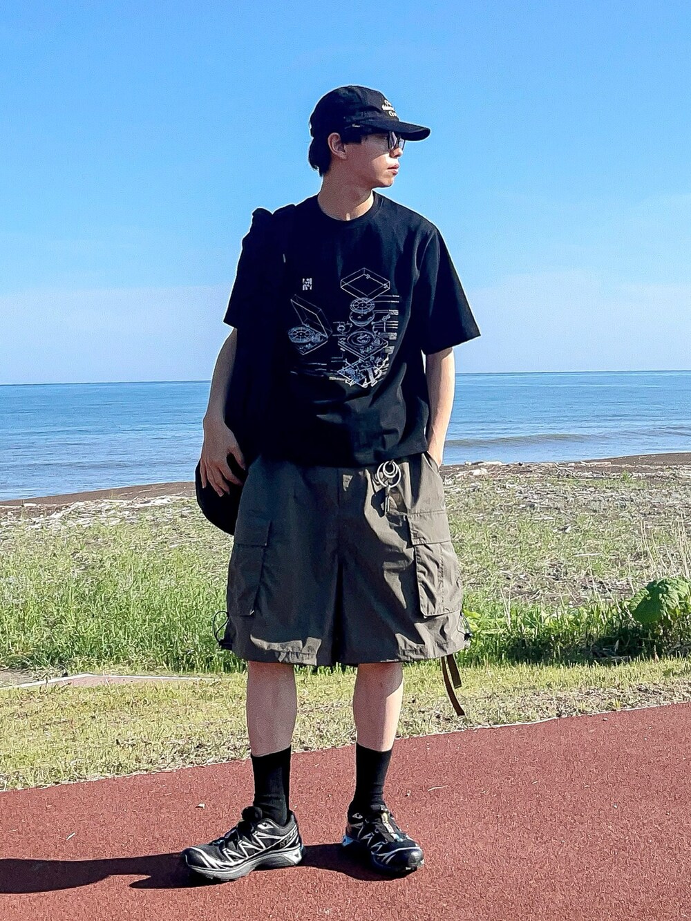 ブラック系のTシャツ/カットソー、グリーン系のカーゴパンツ、ブラック系のスニーカーを着用したメンズの夏コーディネートの2枚目の写真