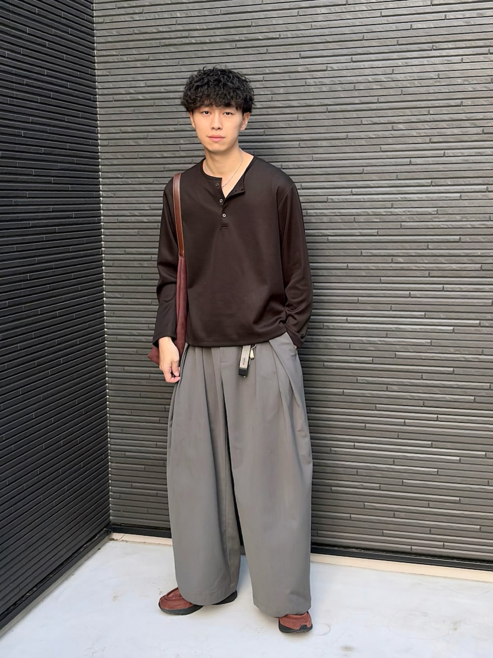 ブラック系のTシャツ/カットソー、グレー系のスラックス、ブラウン系のショルダーバッグを着用したメンズの春コーディネートの3枚目の写真