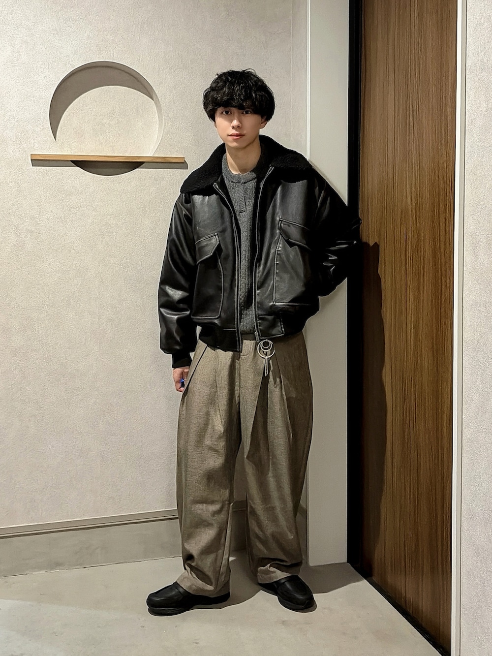 ブラック系のブルゾン、グレー系のニット/セーター、ブラウン系のスラックスを着用したメンズの冬コーディネートの2枚目の写真