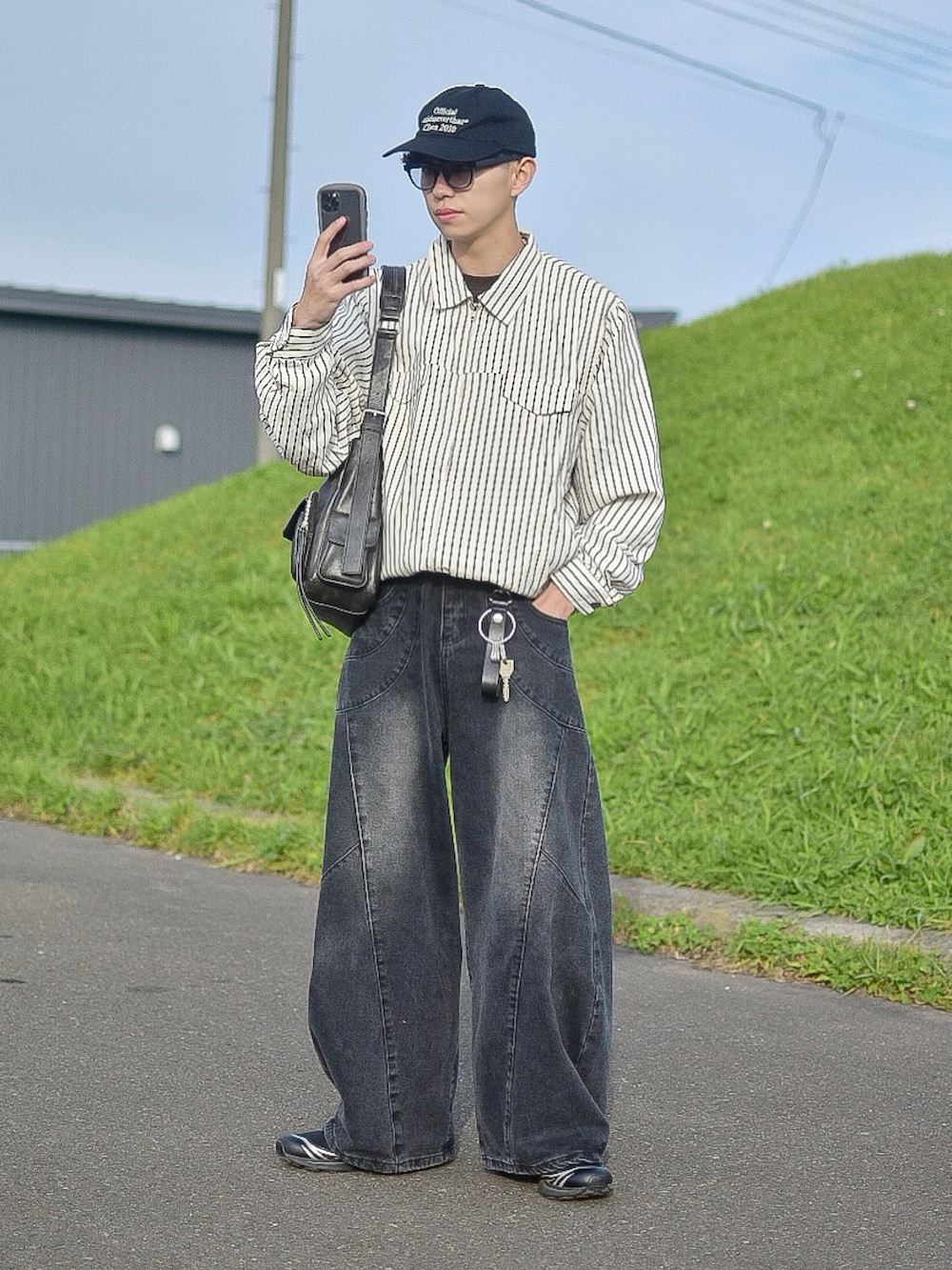 ホワイト系のブルゾン、ブラック系のデニムパンツ、ブラック系のショルダーバッグを着用したメンズの秋コーディネートの2枚目の写真