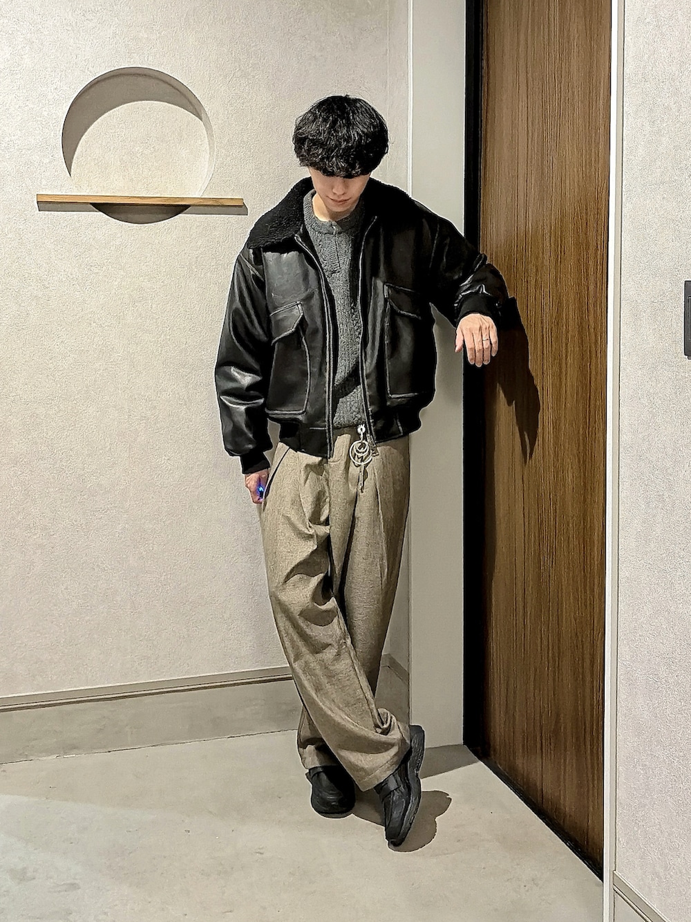 ブラック系のブルゾン、グレー系のニット/セーター、ブラウン系のスラックスを着用したメンズの冬コーディネートの3枚目の写真