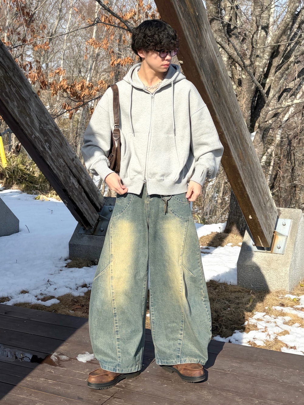 グレー系のパーカー、ブルー系のデニムパンツ、ブラウン系のブーツを着用したメンズの春コーディネートの2枚目の写真