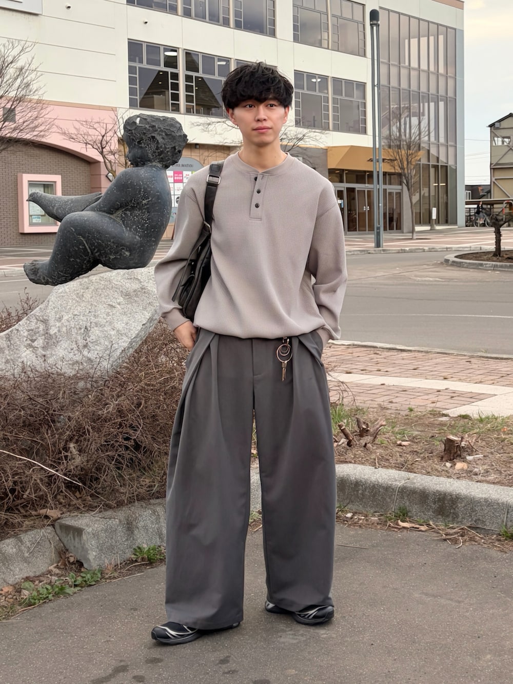 グレー系のTシャツ/カットソー、グレー系のスラックス、ブラック系のショルダーバッグを着用したメンズの春コーディネートの2枚目の写真