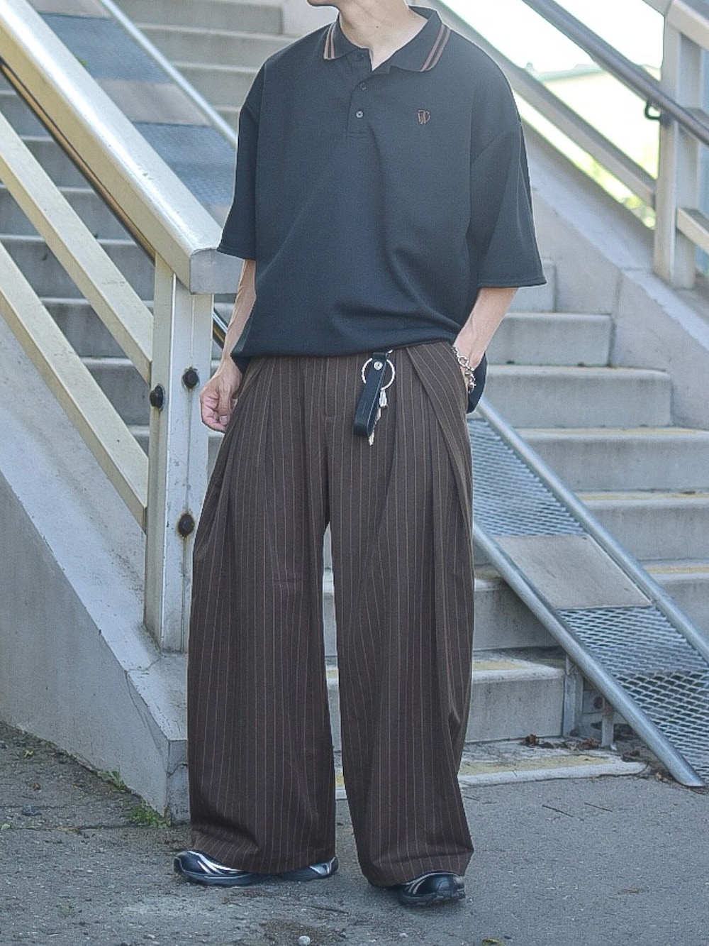 ブラック系のポロシャツ、ブラウン系のスラックス、ブラック系のスニーカーを着用したメンズの夏コーディネートの2枚目の写真