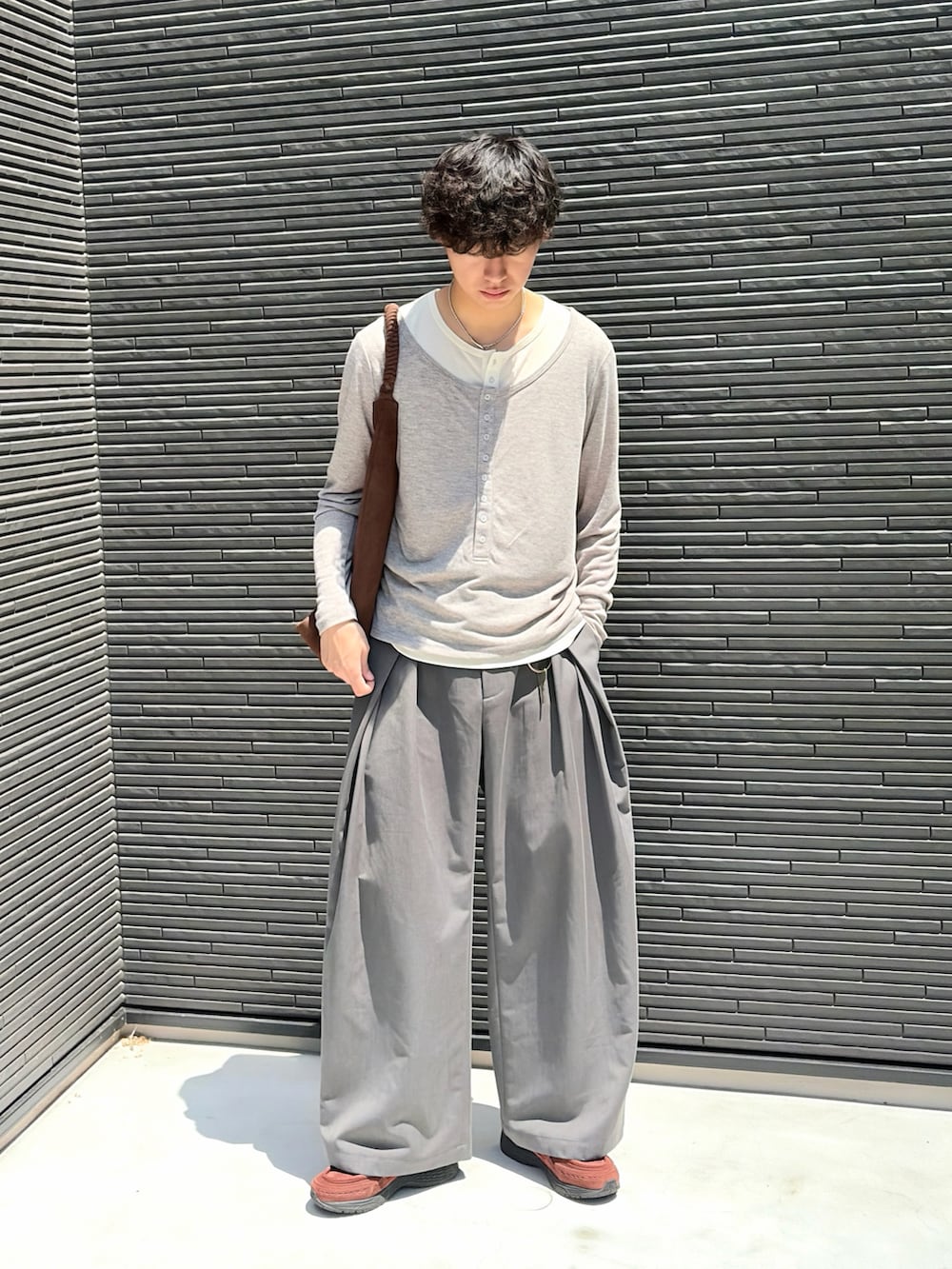 ブラウン系のトートバッグ、グレー系のTシャツ/カットソー、グレー系のスラックスを着用したメンズの夏コーディネートの3枚目の写真
