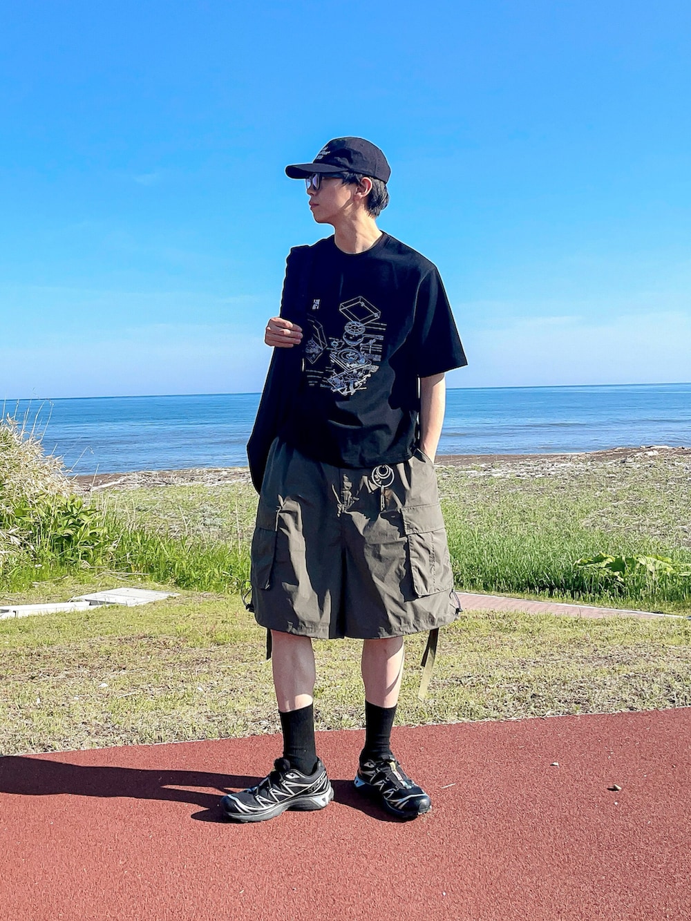 ブラック系のTシャツ/カットソー、グリーン系のカーゴパンツ、ブラック系のスニーカーを着用したメンズの夏コーディネートの3枚目の写真