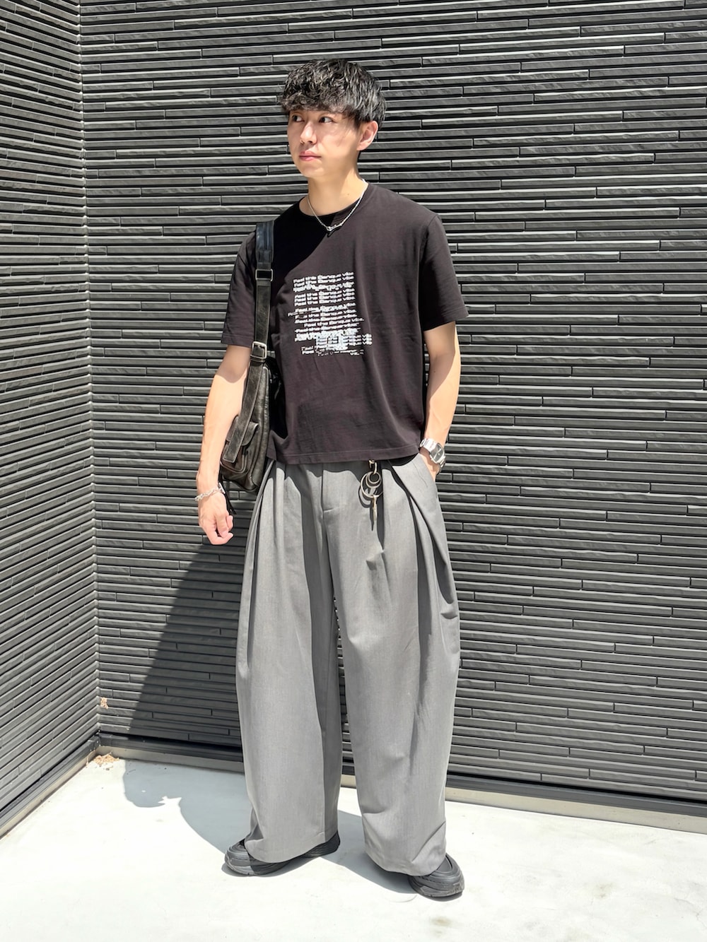 ブラック系のTシャツ/カットソー、グレー系のスラックス、ブラック系のショルダーバッグを着用したメンズの夏コーディネートの3枚目の写真