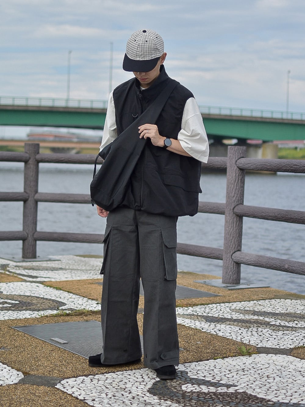 ブラック系のベスト、ブラック系のショルダーバッグ、グレー系のカーゴパンツを着用したメンズの夏コーディネートの2枚目の写真