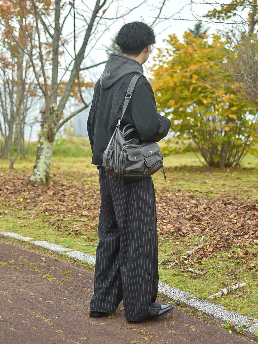 グレー系のパーカー、ブラック系のブルゾン、ブラック系のスラックスを着用したメンズの秋コーディネートの4枚目の写真