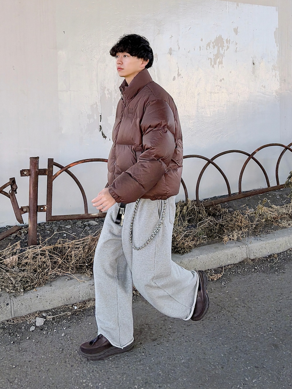 ブラウン系のダウンジャケット/コート、ブラウン系のニット/セーター、グレー系のスウェットパンツを着用したメンズの冬コーディネートの3枚目の写真