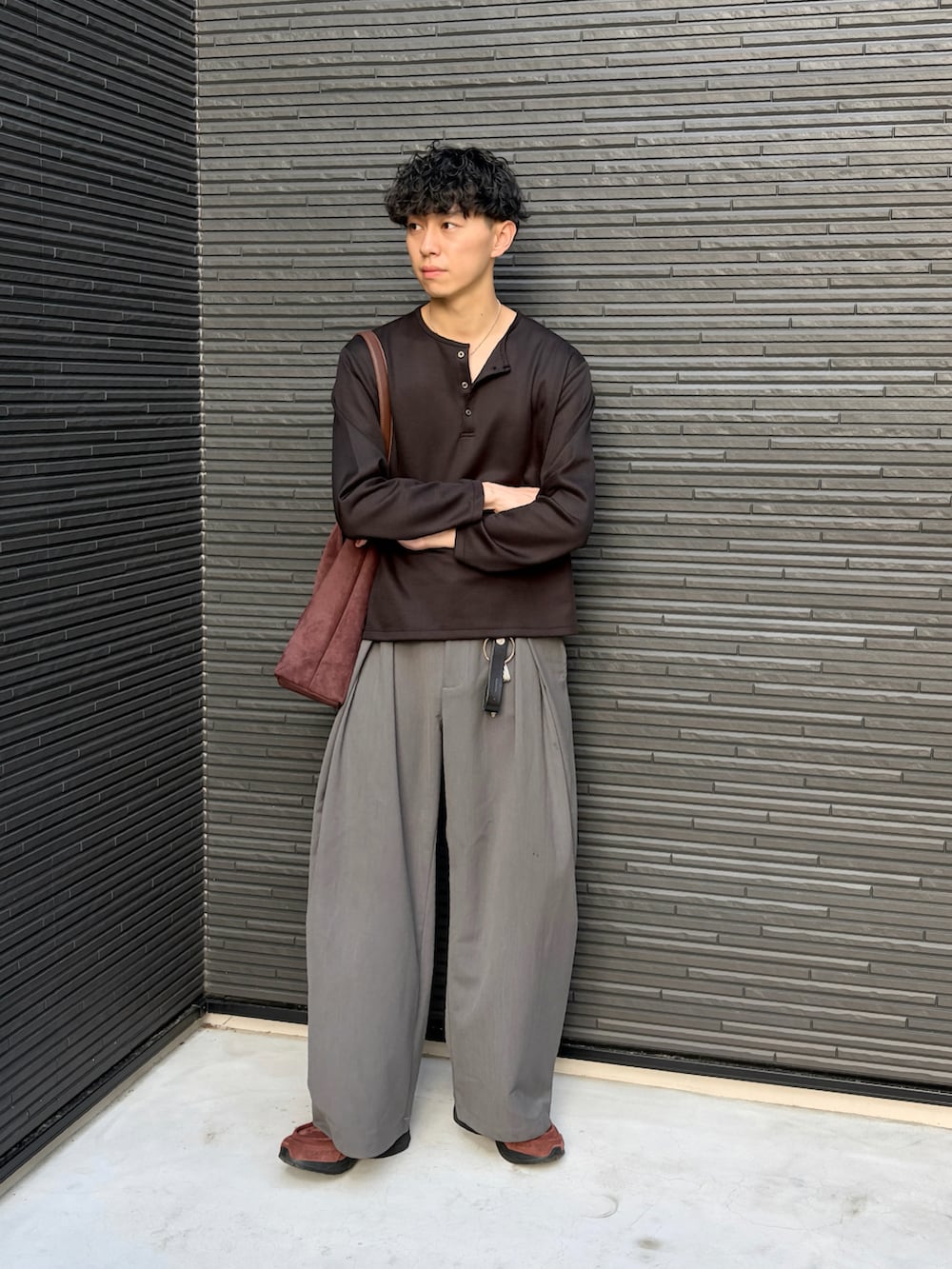 ブラック系のTシャツ/カットソー、グレー系のスラックス、ブラウン系のショルダーバッグを着用したメンズの春コーディネートの2枚目の写真