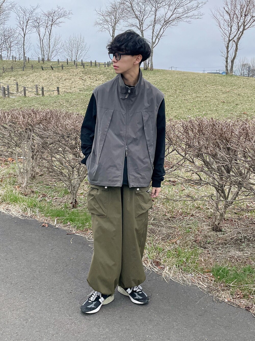 グレー系のベスト、ブラック系のTシャツ/カットソー、グリーン系のカーゴパンツを着用したメンズの春コーディネートの2枚目の写真