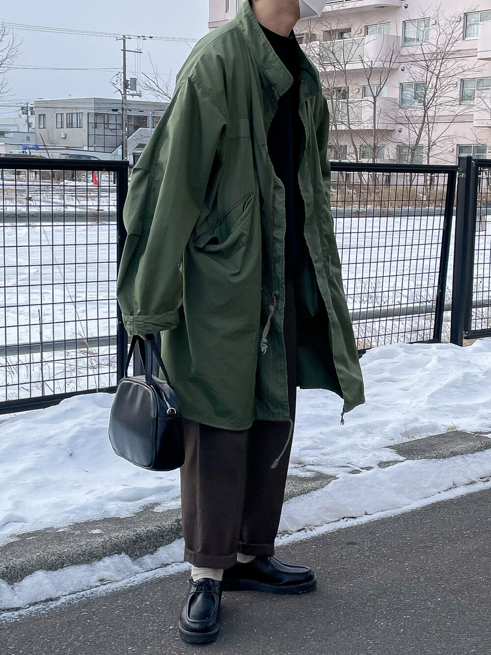 グリーン系のモッズコート、ブラック系のニット/セーター、ブラウン系のパンツを着用したメンズの冬コーディネートの2枚目の写真