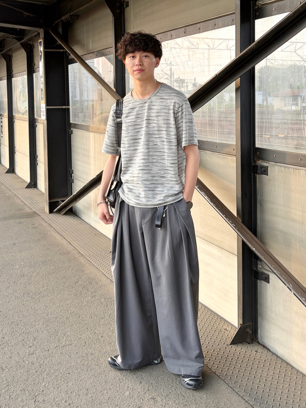 グレー系のTシャツ/カットソー、グレー系のスラックス、ブラック系のショルダーバッグを着用したメンズの春コーディネートの2枚目の写真