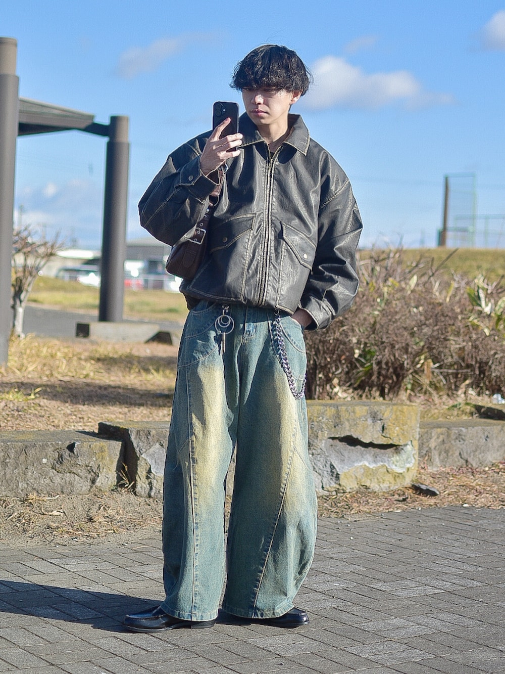 ブラック系のライダースジャケット、ブルー系のデニムパンツ、ブラウン系のハンドバッグを着用したメンズの冬コーディネートの2枚目の写真