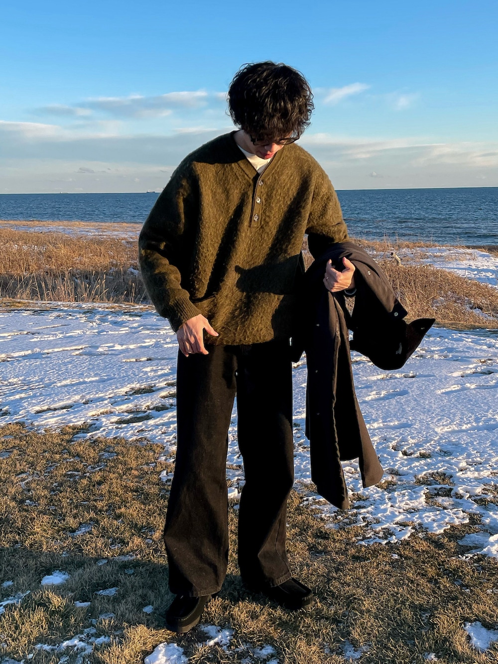 グリーン系のニット/セーター、グレー系のTシャツ/カットソー、ブラック系のデニムパンツを着用したメンズの冬コーディネートの2枚目の写真