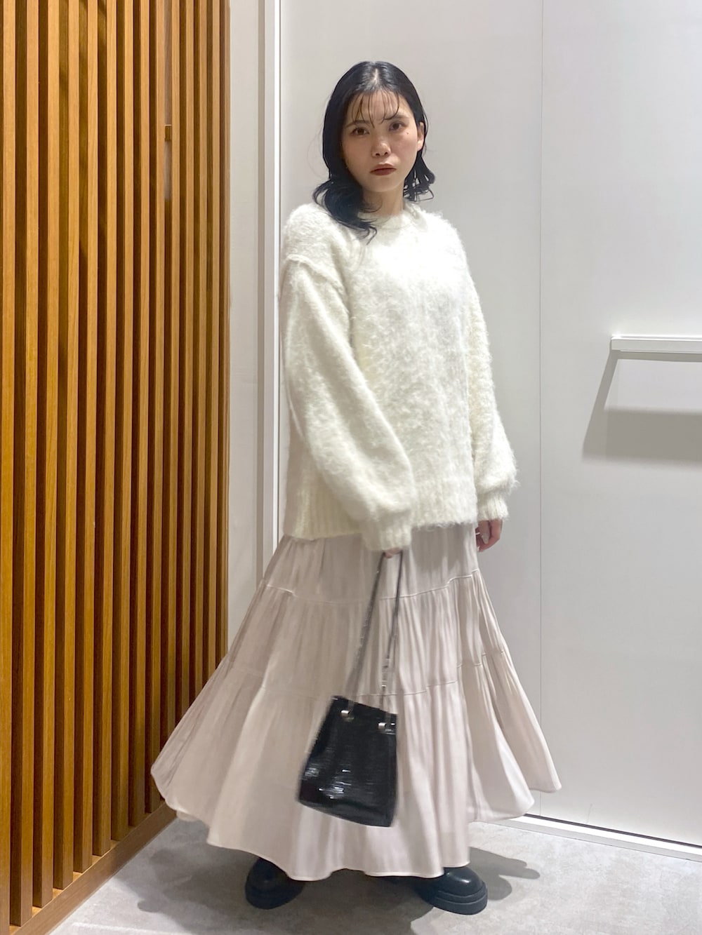 ホワイト系のニット/セーター、ブラック系のショルダーバッグ、ホワイト系のスカートを着用したレディースの冬コーディネートの2枚目の写真