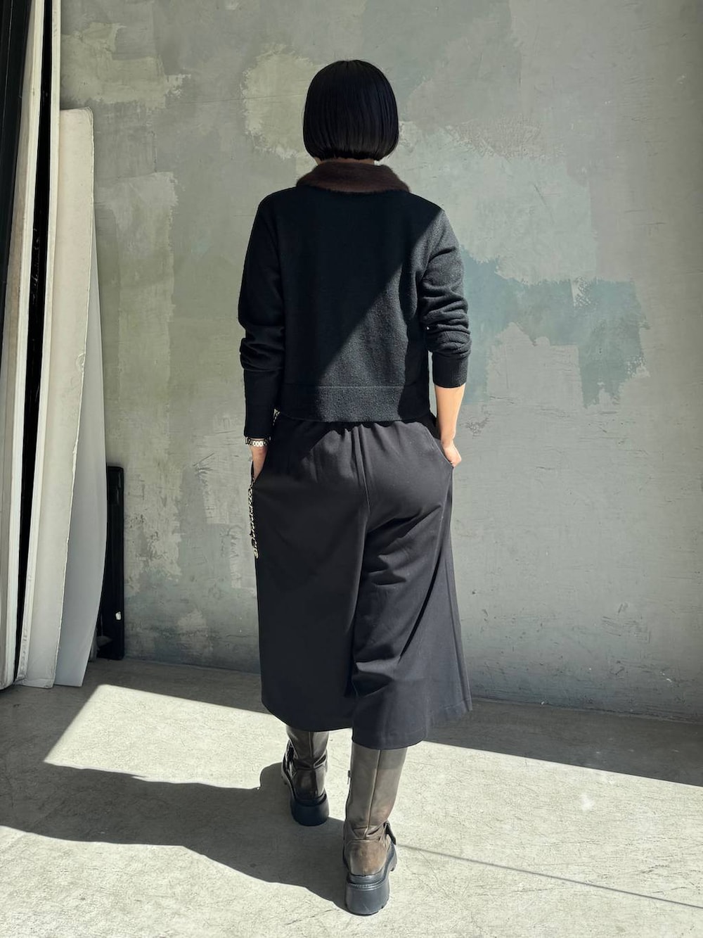 ブラック系のカーディガン/ボレロ、ブラック系のスラックス、ブラウン系のブーツを着用したレディースの秋コーディネートの4枚目の写真